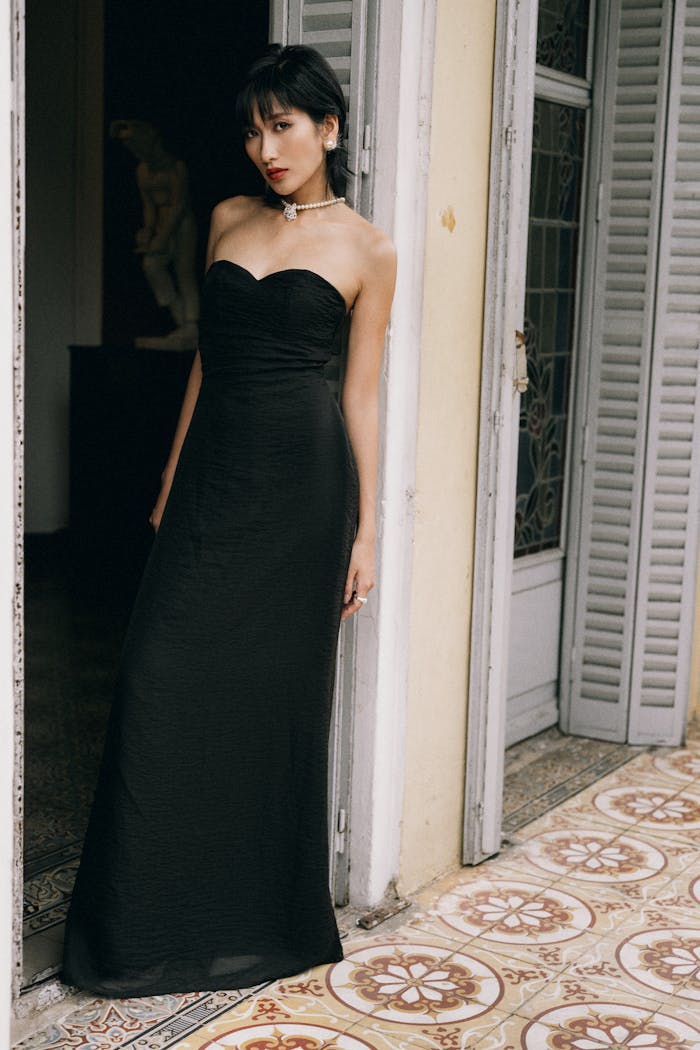 A stylish woman in a black evening gown poses at a vintage doorway, exuding elegance.