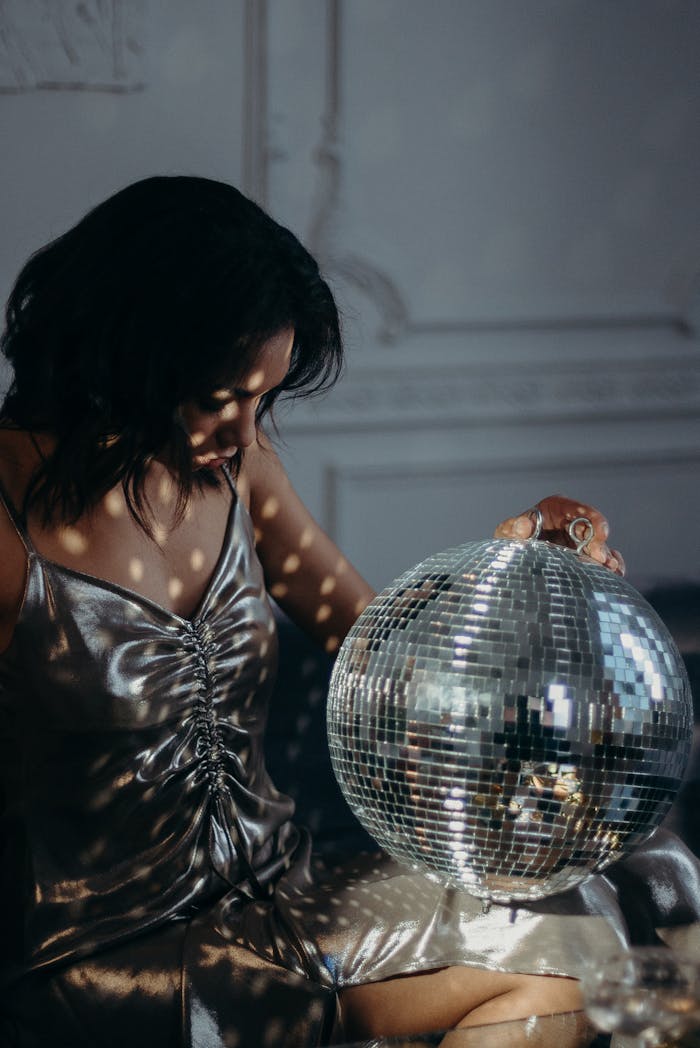 A woman in a silver dress holding a disco ball adds glamour to a chic setting.
