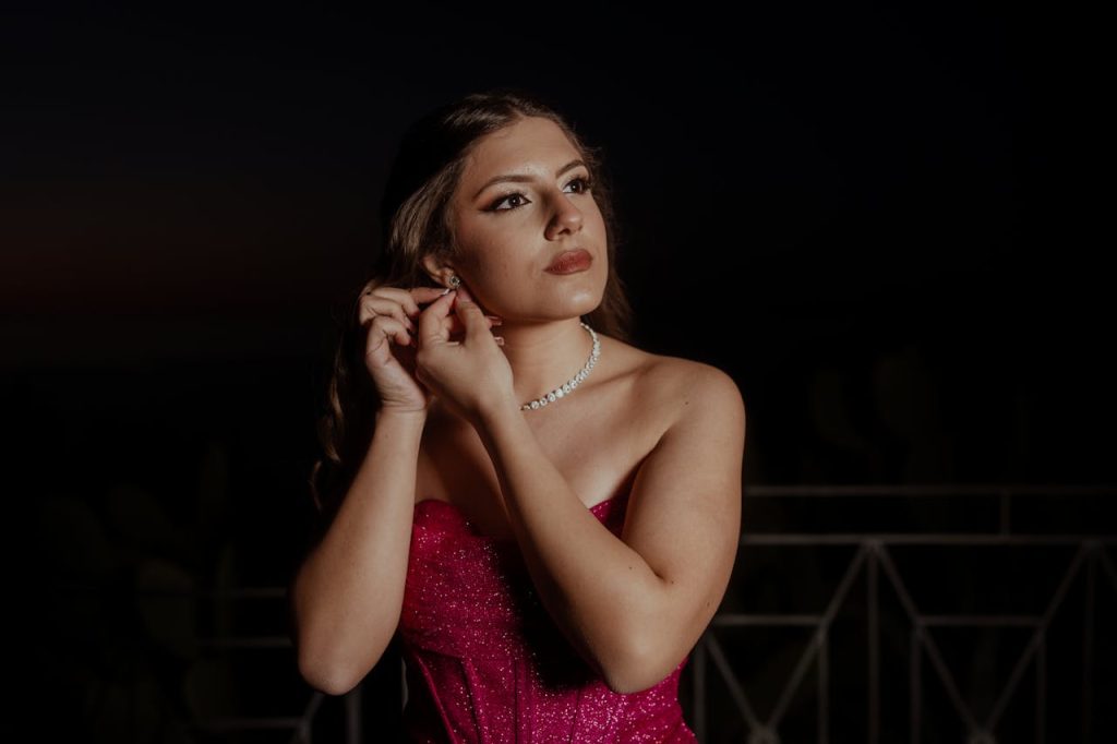 pexels photo 34311636 2 Elegant woman wearing a pink dress adjusting earrings at twilight, exuding grace and glamour.